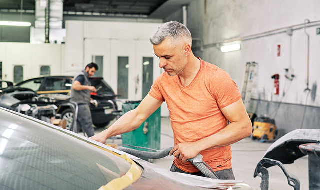 Mechanic in orange shirt works on a car